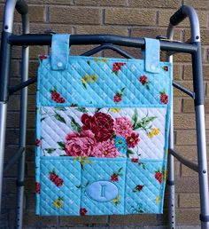 a blue and pink flowered purse hanging on a metal frame next to a brick wall