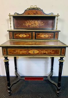 an antique desk with three drawers and gold trimmings on the top, sitting in front of a white wall