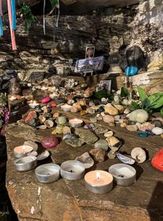 candles and rocks are on the ground in front of a stone wall with pictures hanging from it