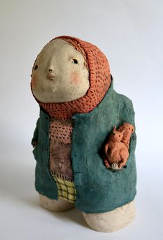 a ceramic figurine with a coat and hat on it's head, holding a teddy bear