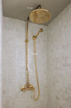 a shower head and hand shower in a white tiled bathroom with gold faucet