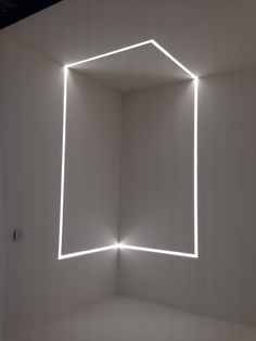 an empty room with white walls and neon lights on the wall, as well as a square shaped light fixture