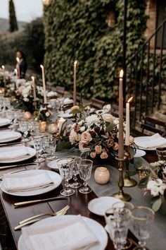 a long table is set with white plates and silverware for an elegant dinner party