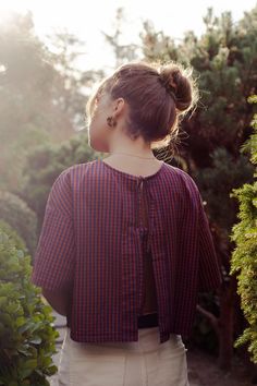 a woman standing in front of bushes and trees with her back turned to the camera