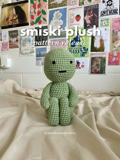 a green crocheted stuffed animal sitting on top of a bed next to a wall covered in pictures