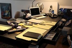 the desk is cluttered with papers and laptops, books, pens, and other office supplies