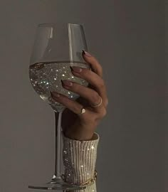 a woman's hand holding a wine glass in front of her face with glitter on it