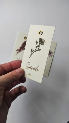 a person holding up two tags with flowers on them