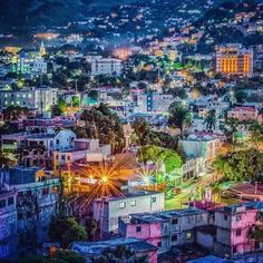 an aerial view of a city at night with lights and buildings in the foreground