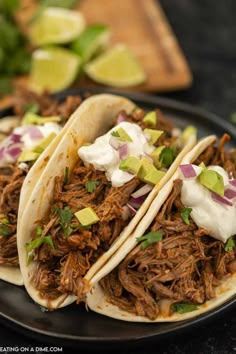 three pulled pork tacos on a plate with sour cream and avocado garnish