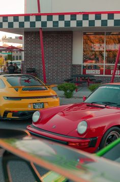 two cars are parked in front of a fast food restaurant, one is red and the other is yellow