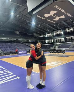 two young women hugging each other on a court in an indoor basketball arena with lights overhead