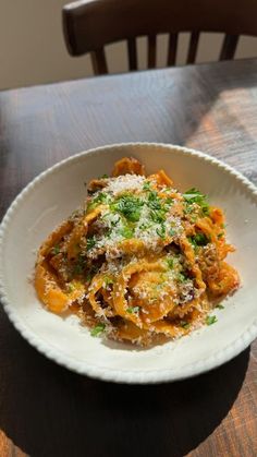 a white bowl filled with pasta covered in sauce and parmesan cheese on top of a wooden table