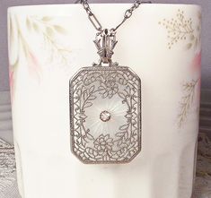 a white vase with a silver necklace on it's neck and an ornate design