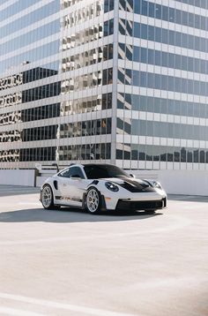 a black and white sports car parked in front of a tall building with glass windows