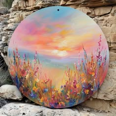 a painting on a rock with flowers in the foreground and a sunset in the background