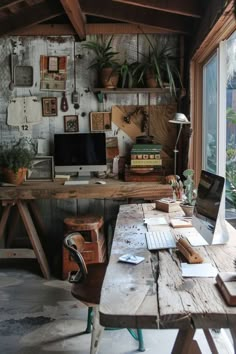 an old desk with two computers on it in front of a window filled with potted plants