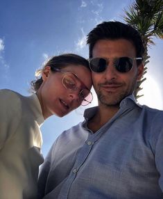 a man and woman wearing sunglasses pose for the camera with palm trees in the background