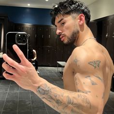 a shirtless man taking a selfie with his cell phone in a public restroom