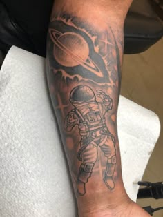 a man's arm with an astronaut tattoo on it and saturn in the background