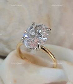 a close up view of a diamond ring on a white marble surface with shells in the background