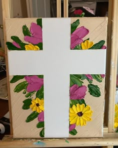 a painted cross with flowers on it sitting in front of a wooden easel,