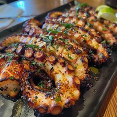 grilled octopus on a black plate with lemon wedges and garnishes