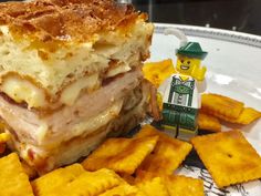 a lego man is next to a sandwich on a plate with cheesy crackers