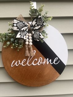 a welcome sign hanging on the side of a house with greenery and beads attached to it