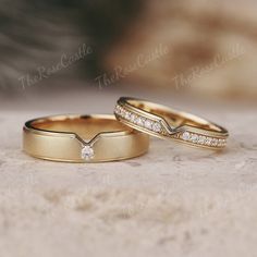 two gold wedding bands with diamonds on them sitting on a stone surface in front of the camera