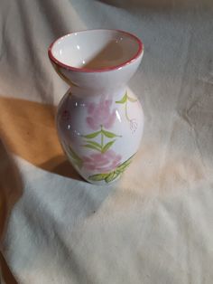 a small white vase sitting on top of a table next to a cloth covered floor