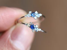 a close up of a person's hand holding a blue and white diamond ring