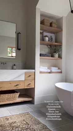 a white bath tub sitting under a bathroom mirror next to a wooden shelf filled with towels