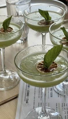 four glasses filled with green liquid and garnished with leafy leaves on top