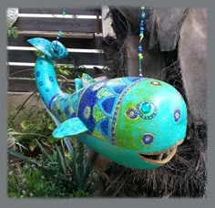 a blue and green painted fish statue next to a wooden bench with beads hanging from it's mouth