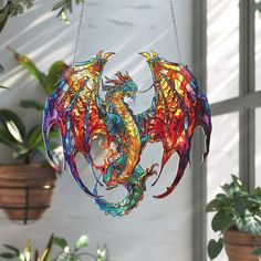 a stained glass dragon ornament hanging from a chain in front of a window