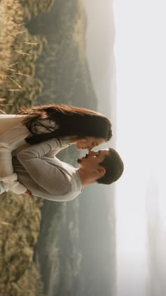 a man and woman standing next to each other in front of a mountain side cliff