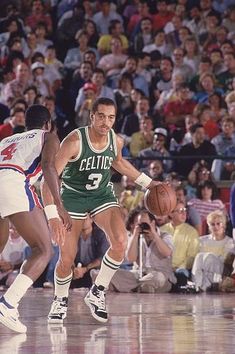 two basketball players in action on the court while people watch from the stands behind them