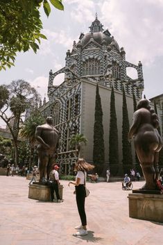 a woman is standing in front of some statues on the ground and buildings behind her