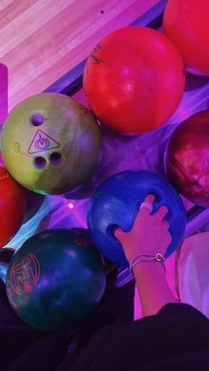 several colorful bowling balls are being held by a person's hand in front of them