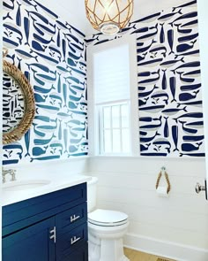 a white toilet sitting next to a bathroom sink under a window in a blue and white wall