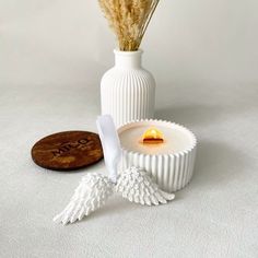 a white vase sitting next to a candle on top of a wooden plate with angel wings around it