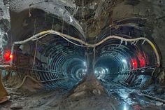 the inside of a tunnel with pipes and wires running through it's center, as well as red lights