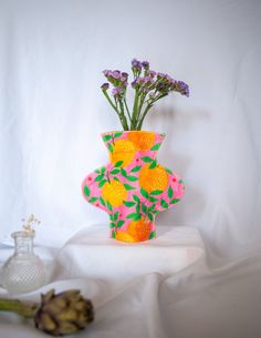 a vase with flowers in it sitting on a white cloth next to a glass bottle