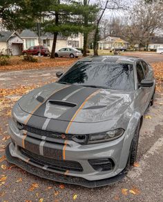 a gray car with orange stripes parked on the side of a road in front of some houses