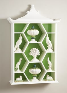 a green shelf with white shelves and vases on it's sides, in front of a wall