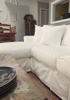 a white couch sitting next to a wooden table with plates on it and a chandelier hanging from the ceiling