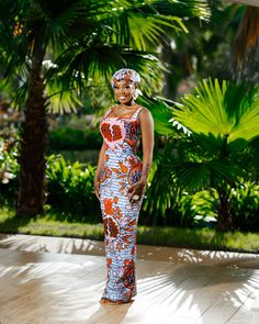 a woman in a colorful dress standing on a wooden floor with palm trees behind her