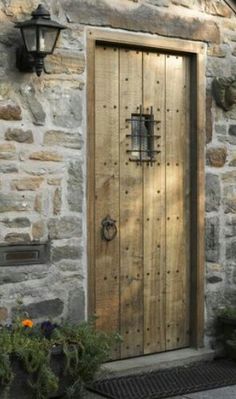 a wooden door in front of a stone building with potted plants next to it