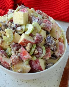 a white bowl filled with fruit salad next to a red towel and wooden spoons